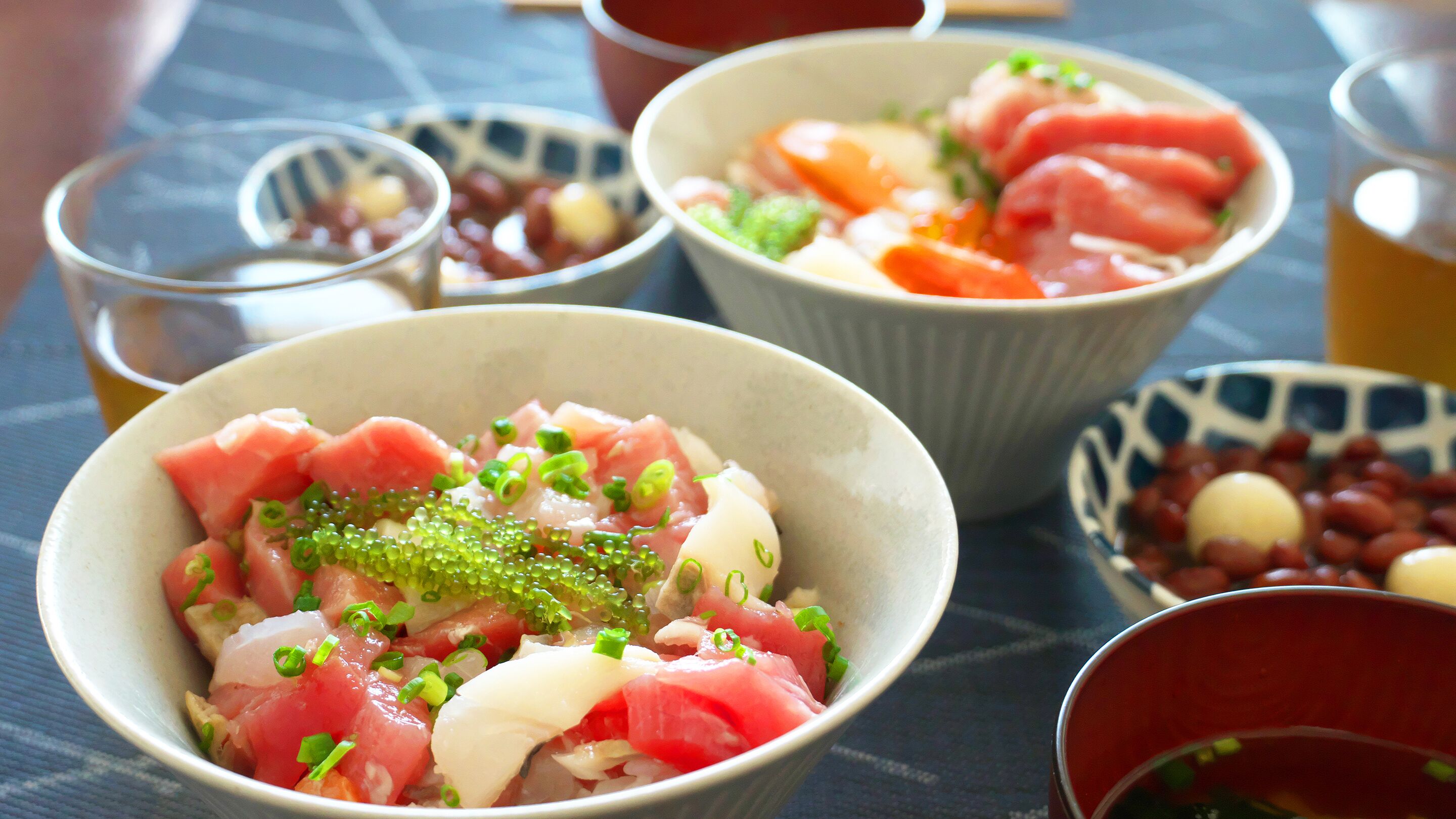Uma mesa com tigelas de comida, incluindo sashimi e outros pratos, e copos de um líquido transparente, provavelmente chá.