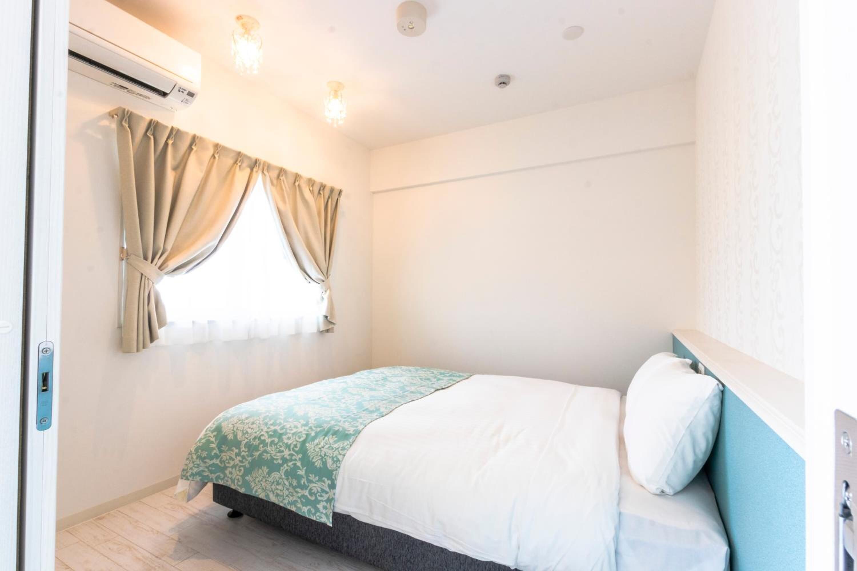 A bedroom with a bed, a window with curtains, an air conditioning unit, and a light fixture.