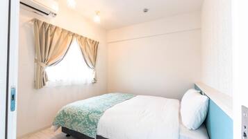 Un dormitorio con cama, ventana con cortinas, unidad de aire acondicionado e iluminación.