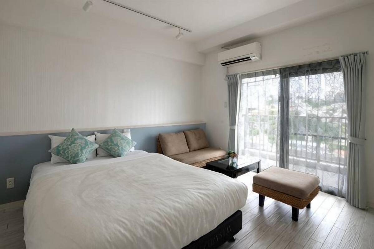 A hotel room with a large bed, a small sofa, a bench, and a large window with curtains.