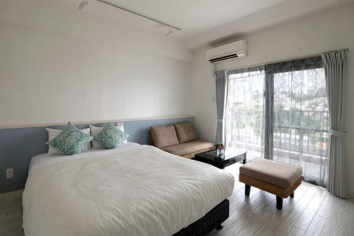 A hotel room with a large bed, a small sofa, a bench, and a large window with curtains.