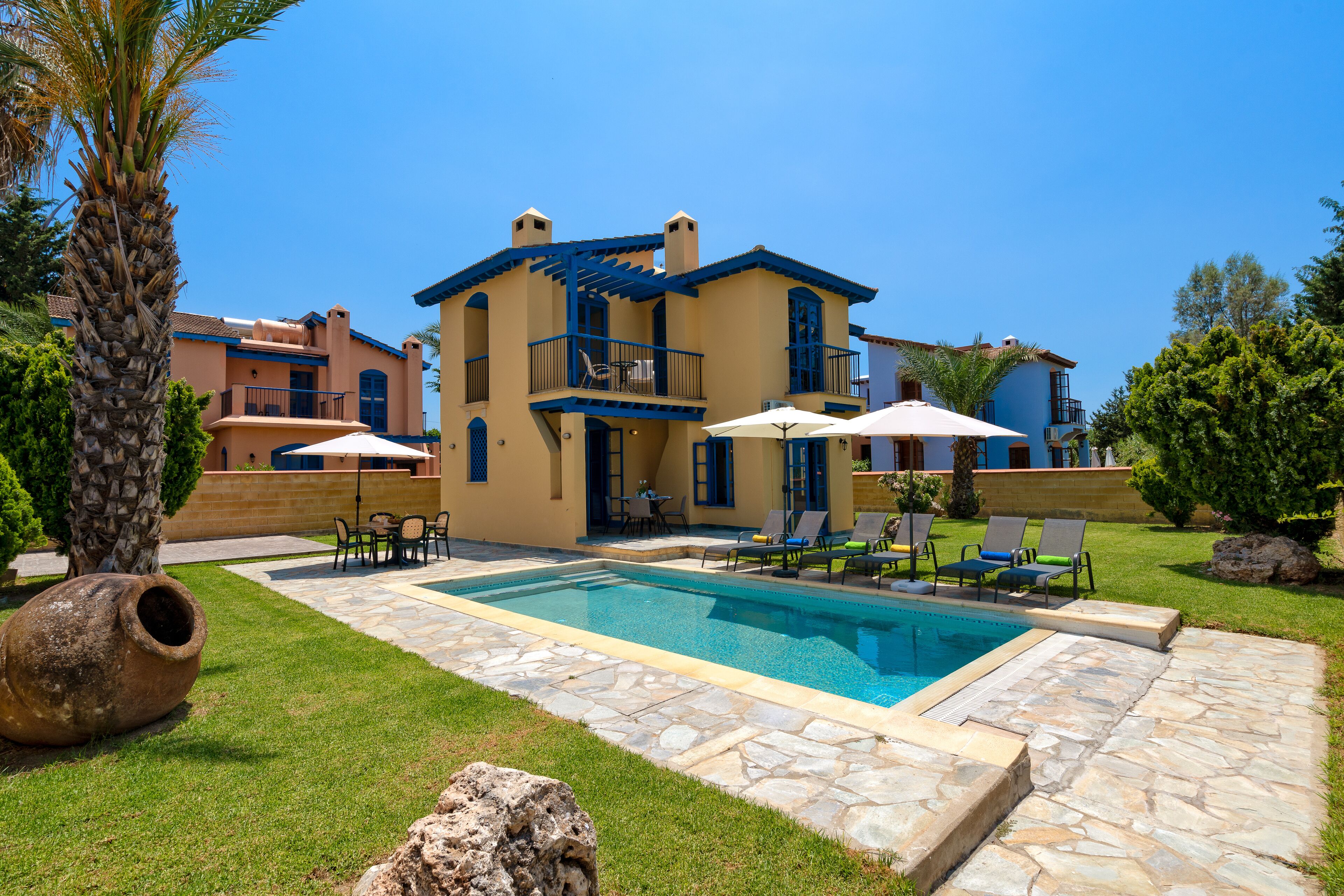 A two-story house with a swimming pool, outdoor furniture, and a stone pathway.