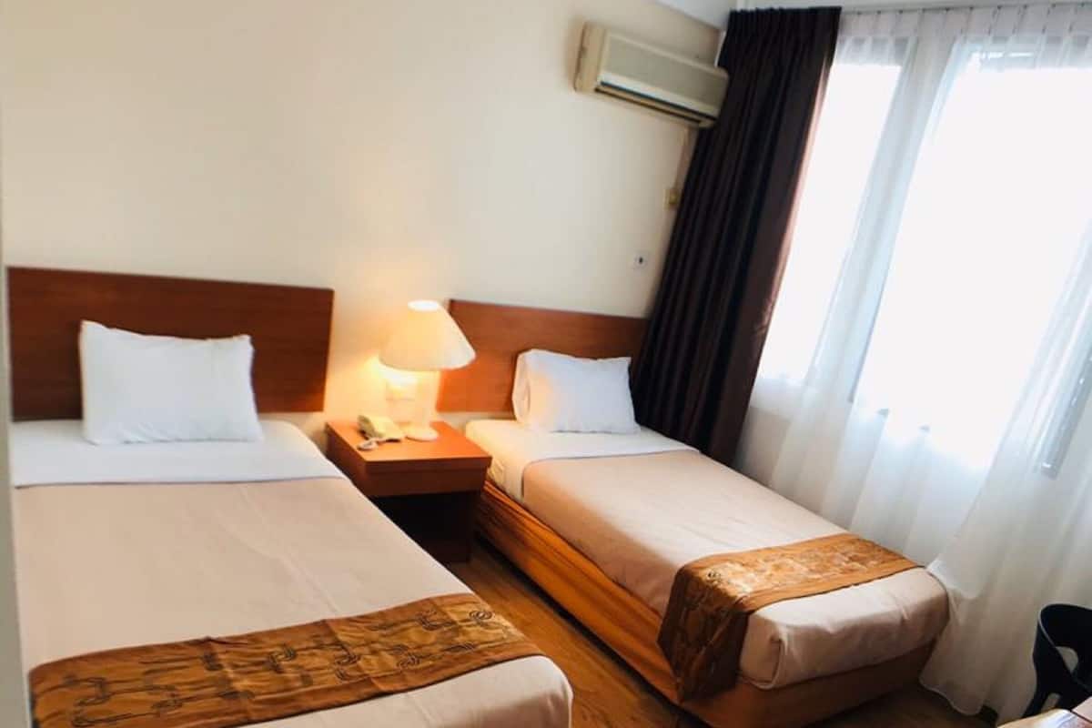 Ett hotellrum med två separata sängar, ett trägolv, ett skrivbord och en luftkonditioneringsanläggning.