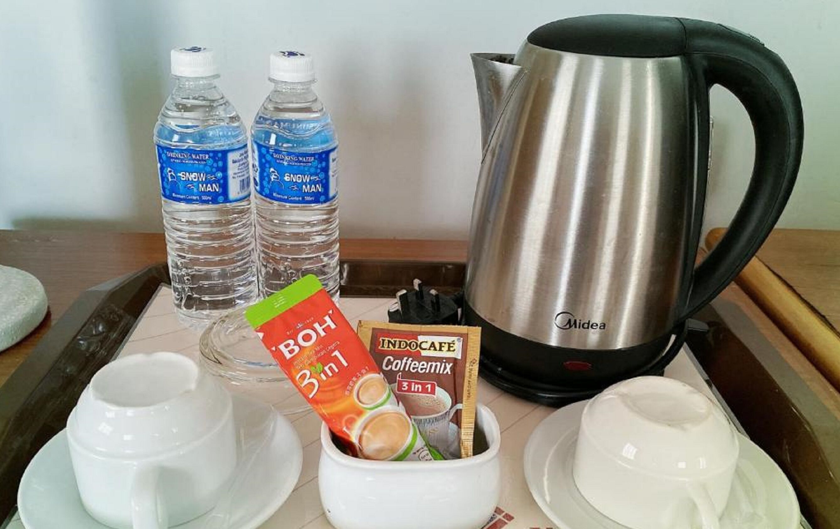 Una bandeja con una tetera, dos botellas de agua, un sobre de mezcla de café y dos tazas.