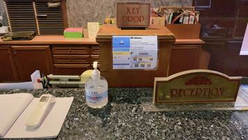 Una recepción con un letrero que dice 'KEY DROP', un aviso de 'Check-in', un dispensador de gel antibacterial y un letrero que indica 'RECEPTION'.