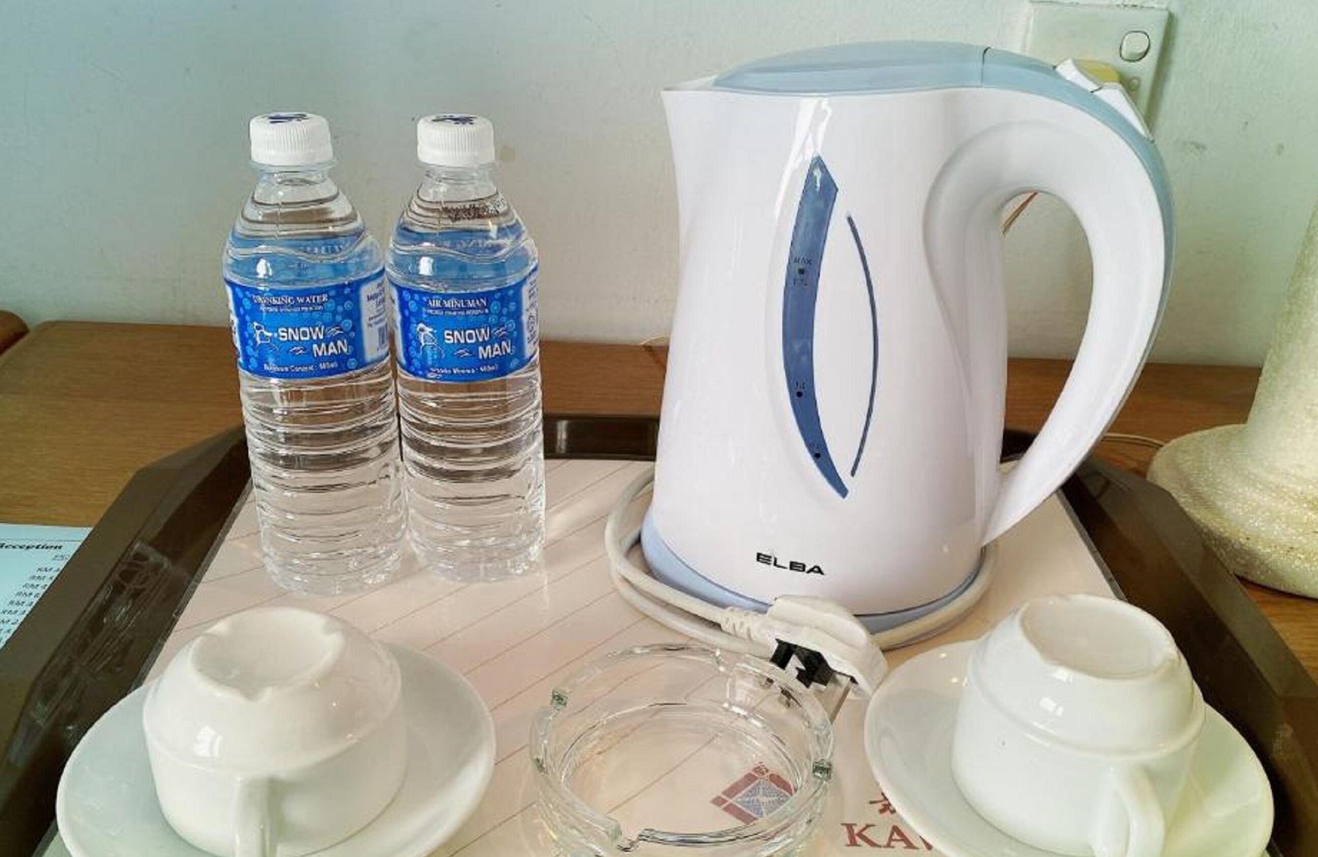A tray with two bottles of Snow Man water, a white Elba electric kettle, and two white cups on a table.