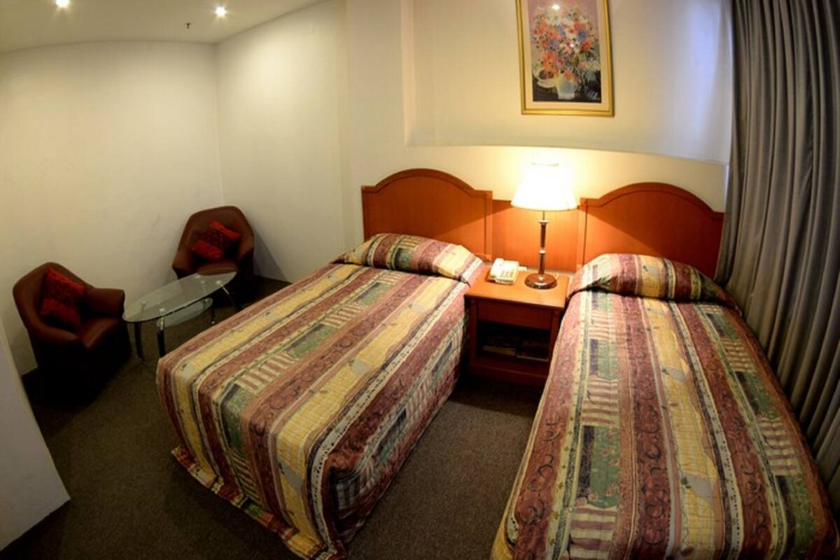 Ett hotellrum med två sängar, ett litet bord, en stol, en lampa och en tavla på väggen.