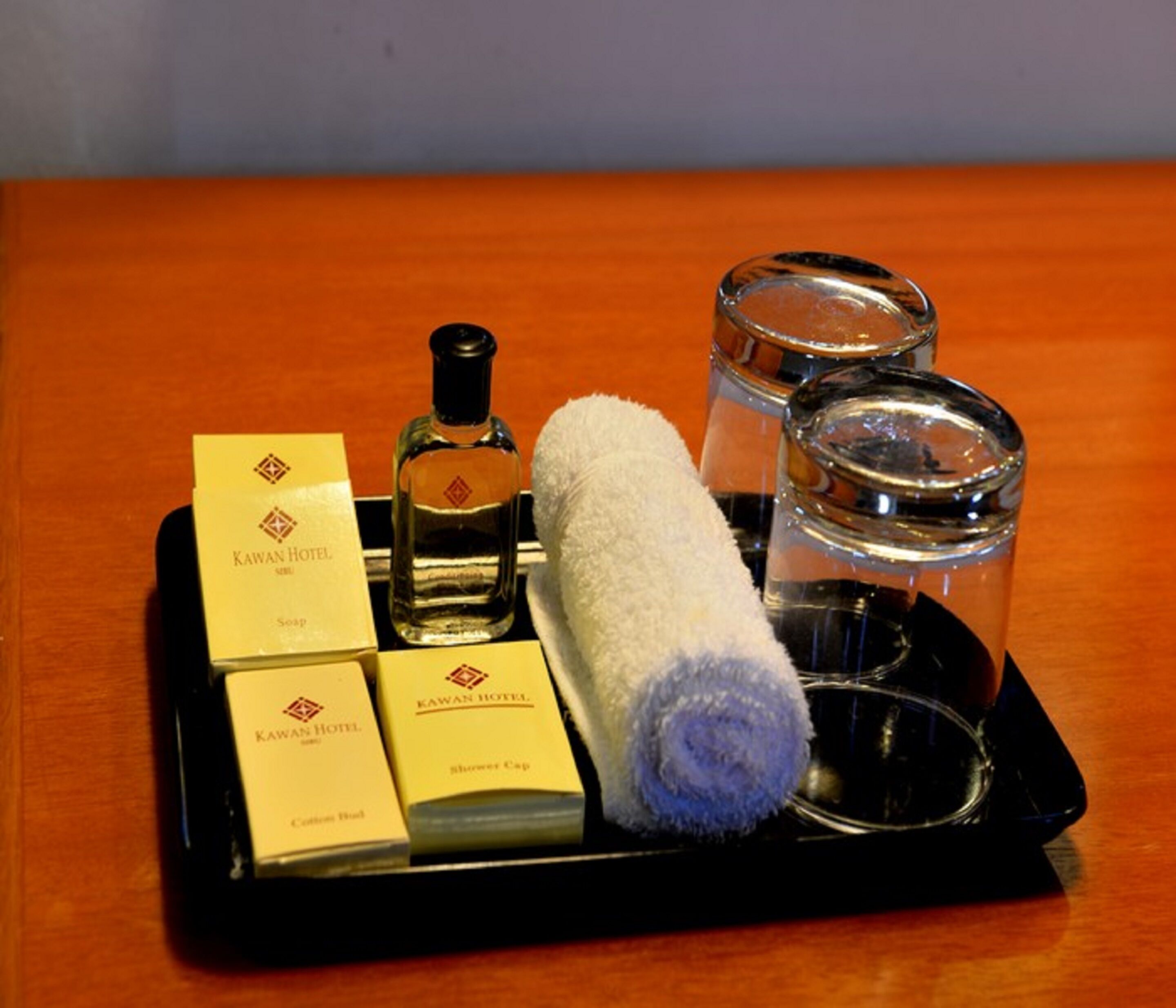 A tray with hotel amenities including a towel, soap, shower cap, and a bottle of perfume.