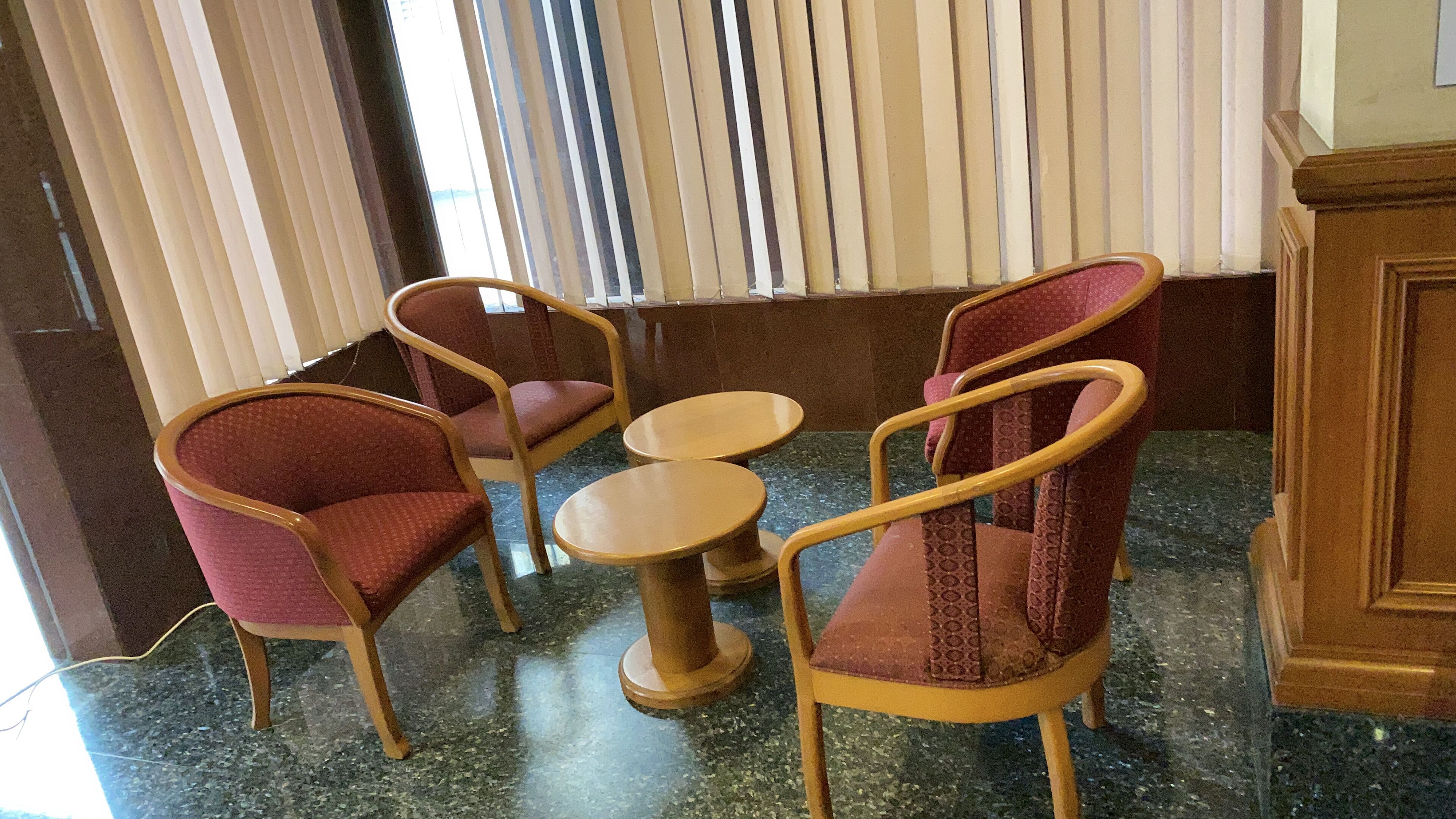 A seating area with four chairs and two round tables, arranged on a polished floor with a window in the background.