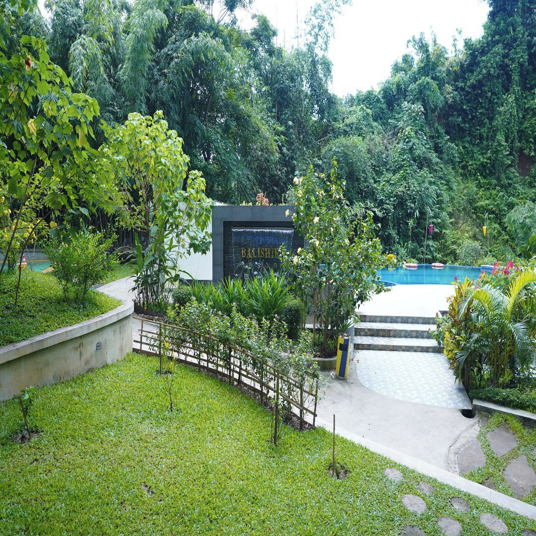 Un exuberante jardín con piscina, un puente de madera y un letrero que dice 'BAISHIN'.