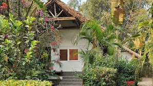 A house with a thatched roof, surrounded by lush greenery and a stone pathway leading to the entrance. - Balishira Resort (Kamalganj)