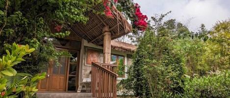 Une maison avec un escalier en bois menant à un porche, entourée d’une végétation luxuriante et de plantes en fleurs.
