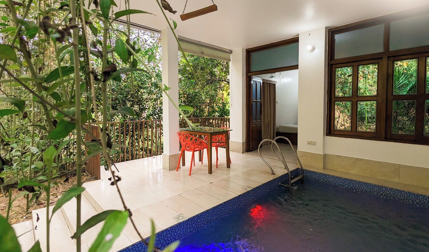 A room with a pool, a table with chairs, and a view of greenery outside.