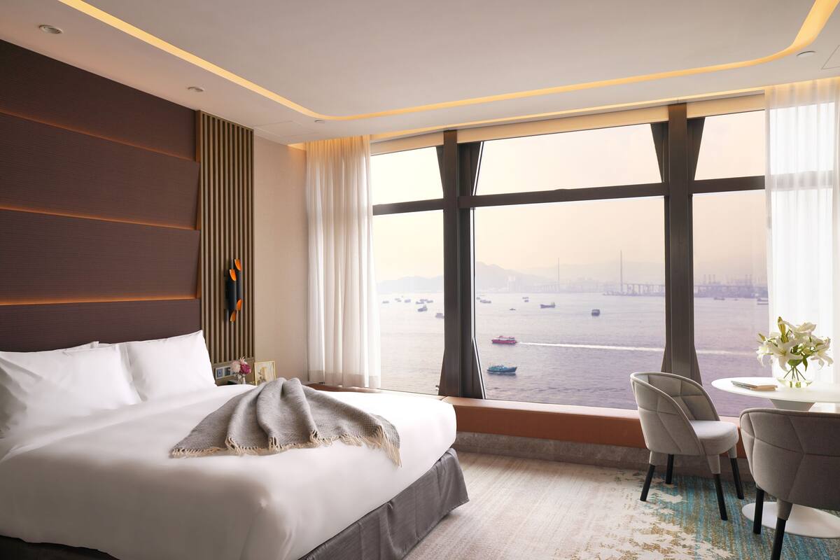 A hotel room with a large bed, a view of the water, and a seating area with two chairs.