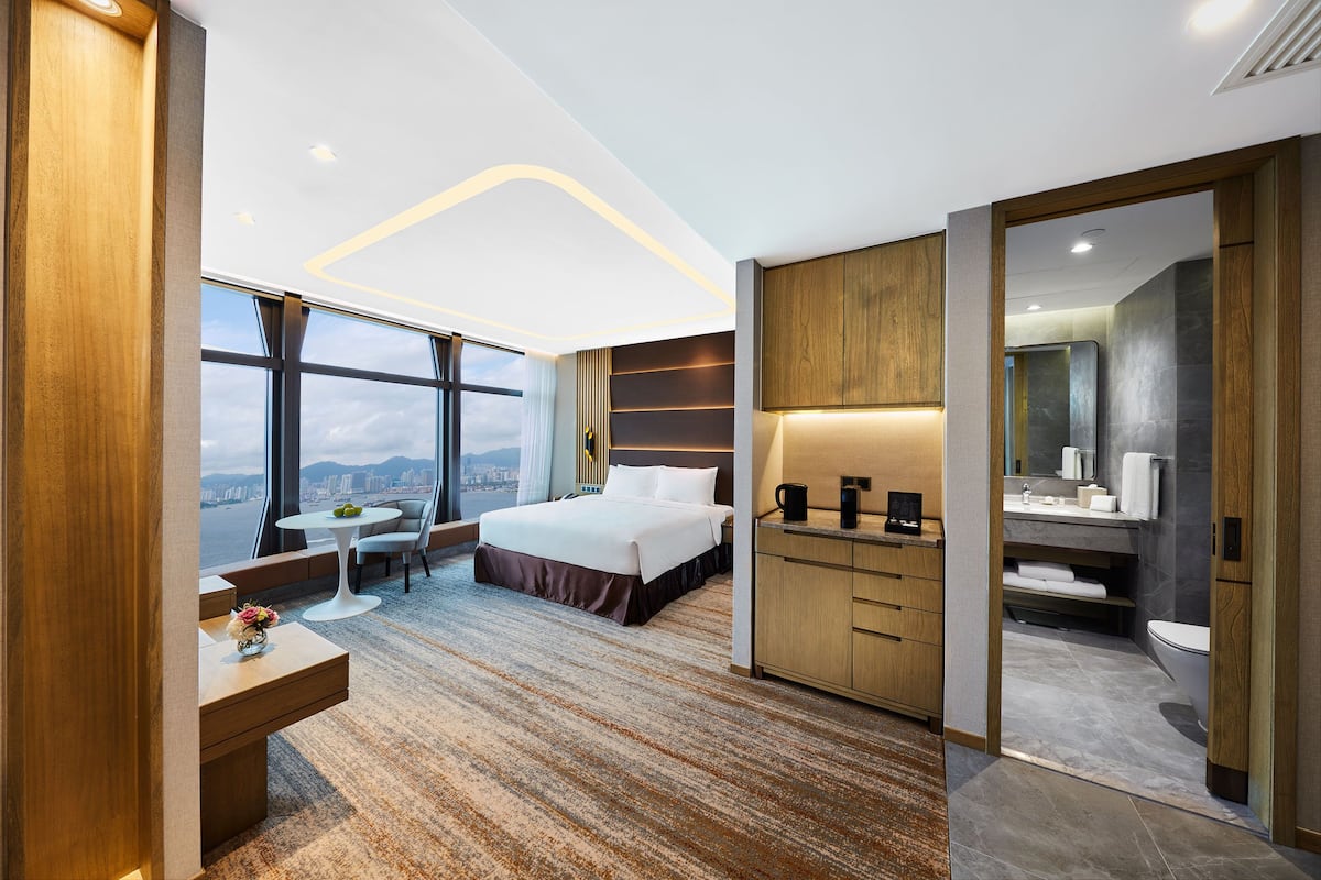A modern hotel room with a large bed, a desk, a small table, and a bathroom.