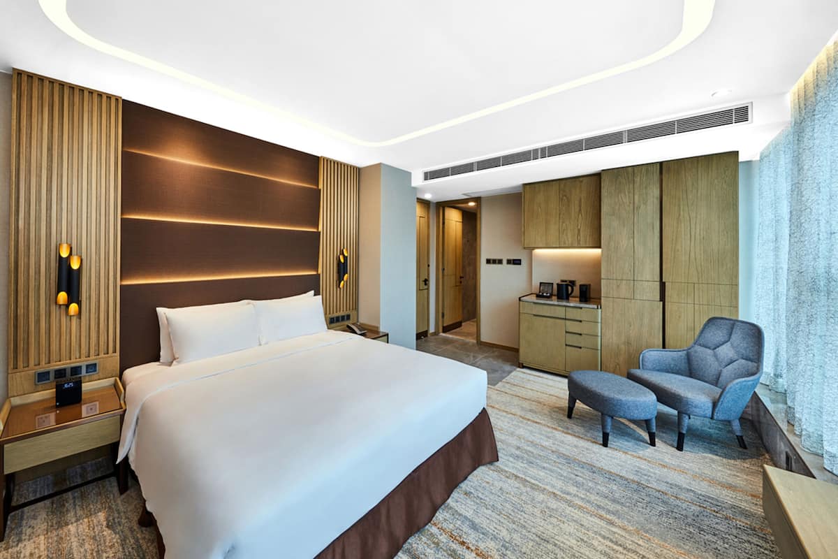 A modern hotel room with a large bed, a desk, a chair, and a wardrobe.