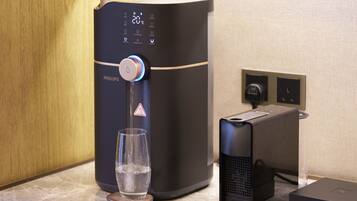 Un distributeur d’eau doté d’un écran numérique, un verre et une machine à café, le tout posé sur un plan de travail.
