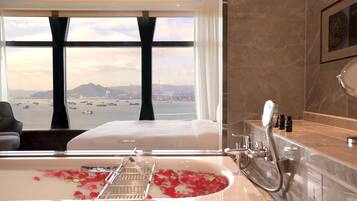 A bathroom with a bathtub filled with rose petals, a large window with a view of a city and mountains, and a modern design with marble countertops.