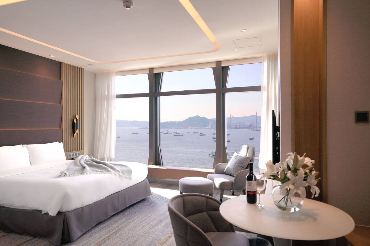 A modern hotel room with a large bed, a seating area, and a view of the water.