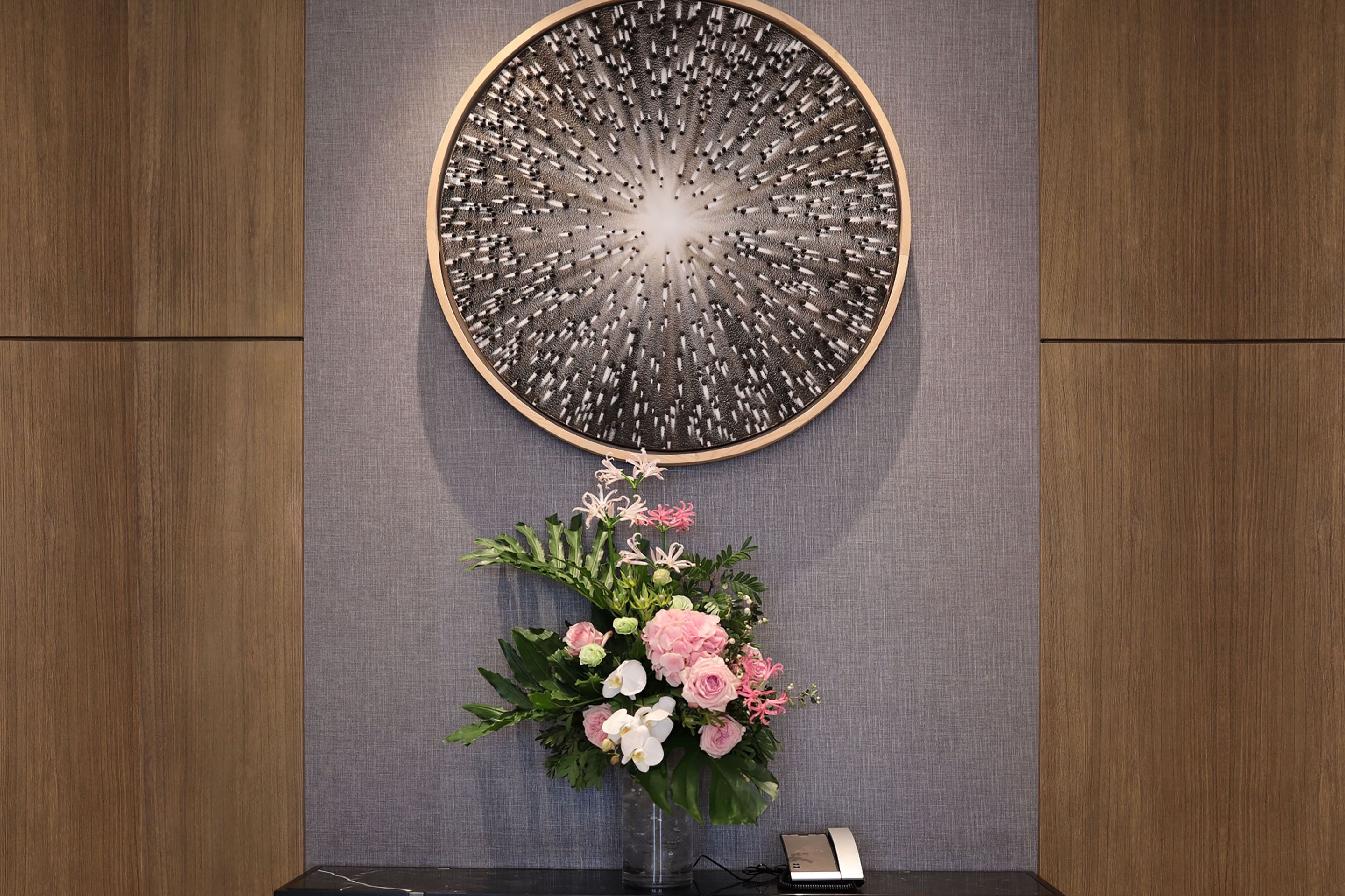 A room with a round wall art piece and a floral arrangement on a table.