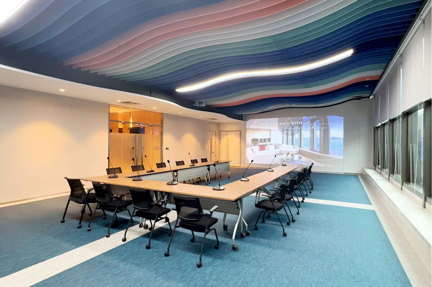 A conference room with a long table, chairs, and a high ceiling with a wavy design.