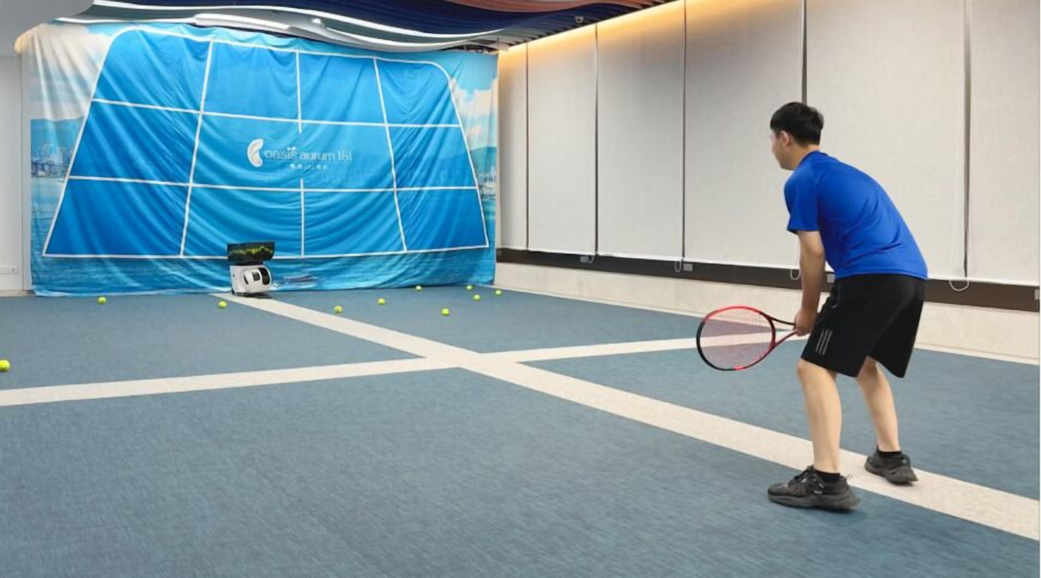 A tennis court with a blue backdrop and a tennis ball machine.