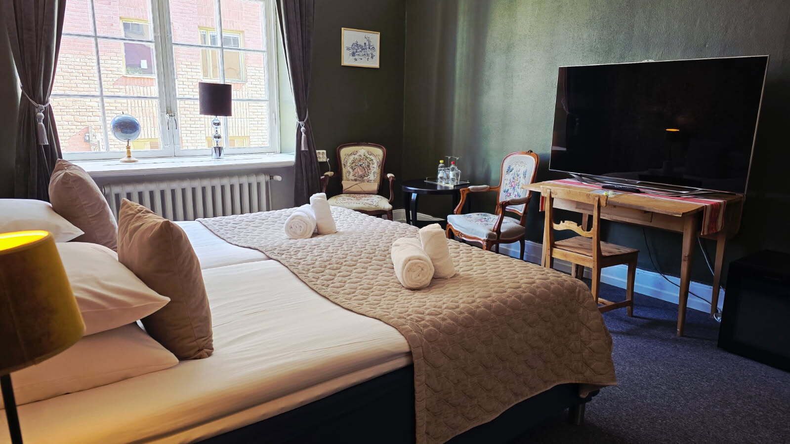 Una habitación de hotel con dos camas, un escritorio, un televisor y una ventana con cortinas.