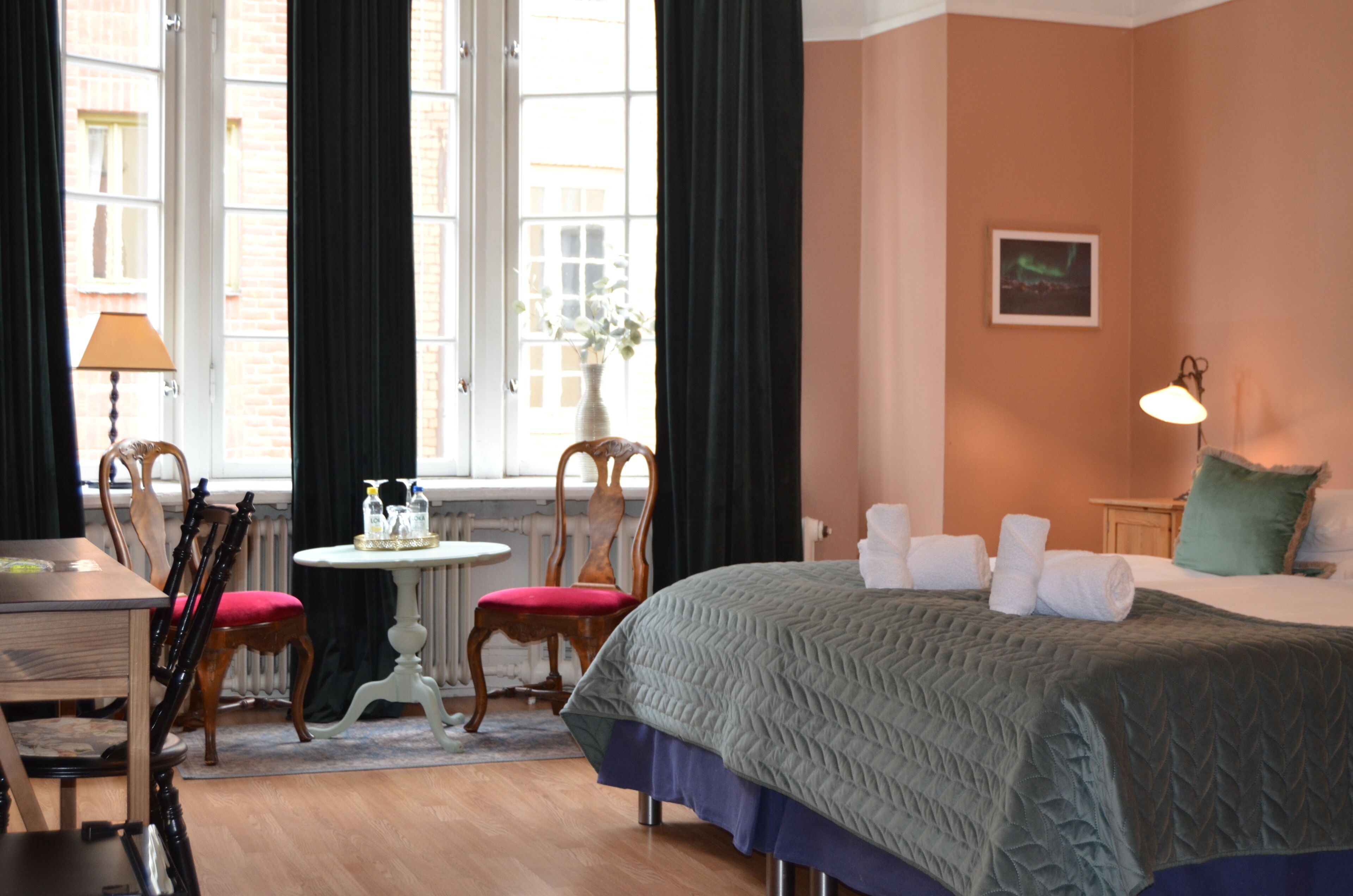 A hotel room with a bed, a table, chairs, a lamp, and a window with curtains.