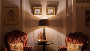 Ein Zimmer mit zwei roten Polstersesseln, einem kleinen runden Tisch mit einer Lampe und gerahmten Bildern an der Wand.