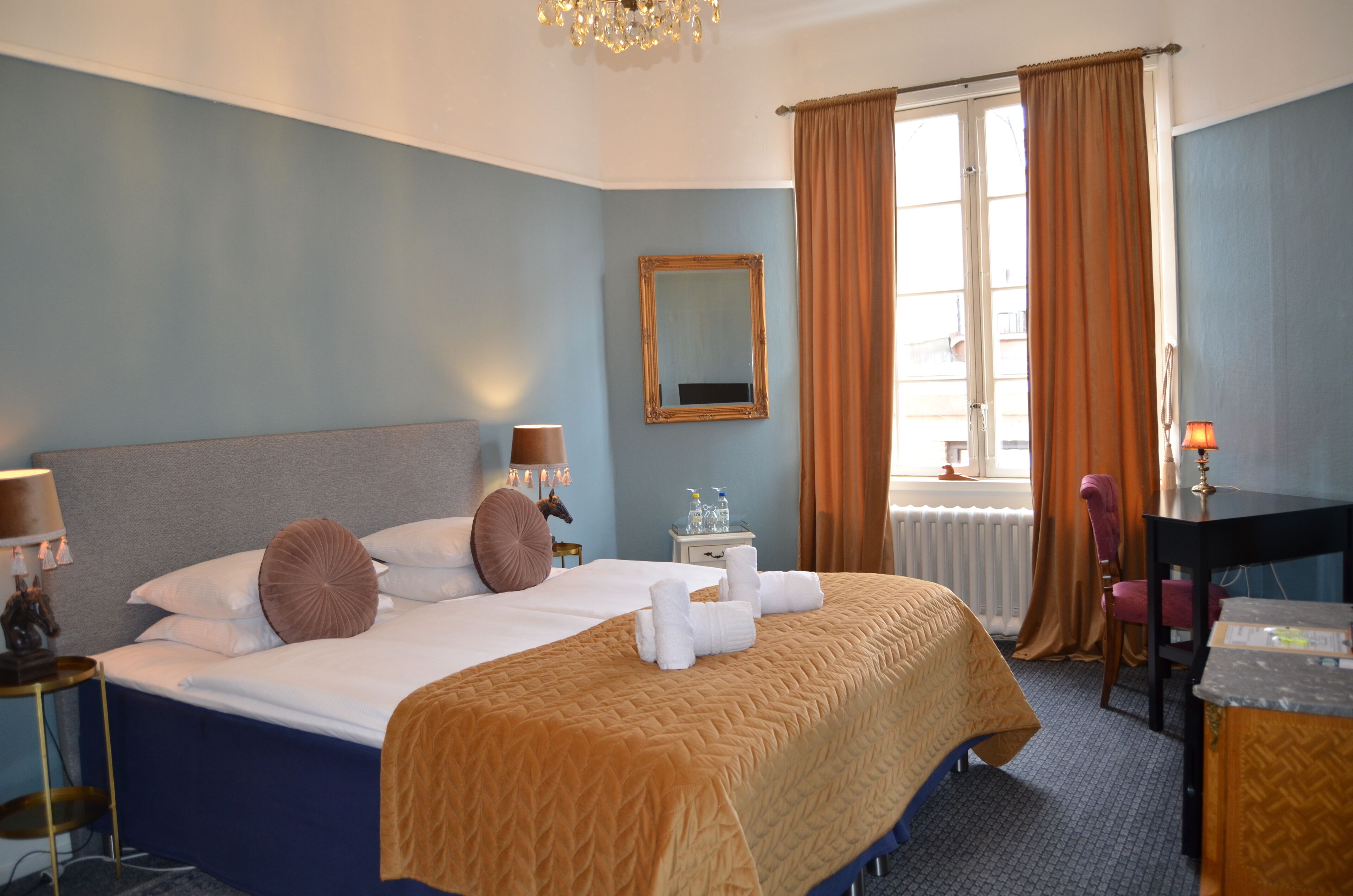 A hotel room with a bed, bedside table, lamp, chair, and a window with curtains.