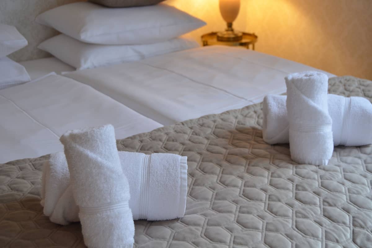 A neatly made bed with white linens and a quilted cover, a bedside lamp, and pillows.