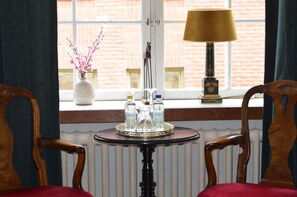 A room with a window, a table with bottles, a lamp, and two chairs.