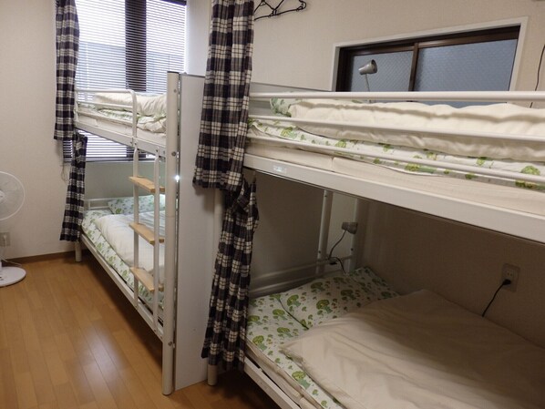 Une chambre de dortoir avec des lits superposés, un ventilateur et une fenêtre avec des stores.