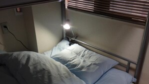 A single bed with a metal frame, a light source above it, and a power outlet on the wall.