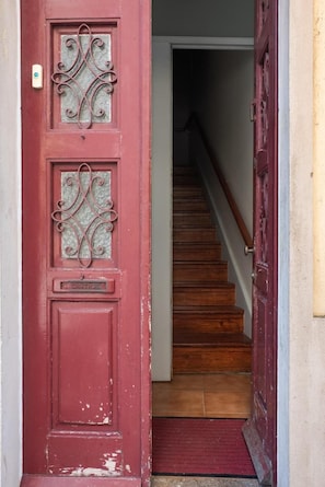 Una puerta roja con una placa, una escalera de madera y un felpudo rojo al pie.