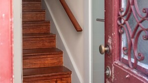 Un escalier en bois mène à une pièce dont la porte est rouge et ornée de motifs en métal.