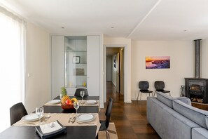 Un salón moderno con un sofá gris, una zona de comedor con una mesa para dos personas y una estufa de leña.