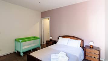 Quarto com cama, berço verde para bebê, duas mesas de cabeceira com abajures e uma porta.