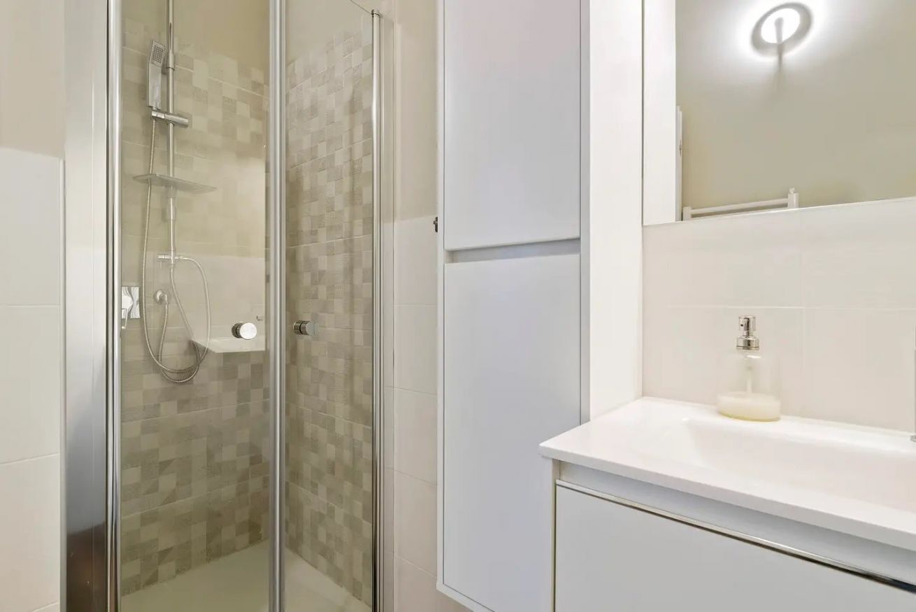 Une salle de bain moderne avec une douche en verre, un lavabo blanc et un miroir avec éclairage intégré.