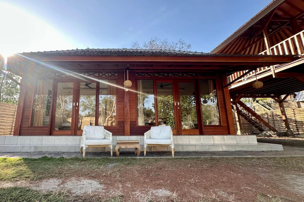 A wooden building with large windows, a covered porch, and two white chairs.