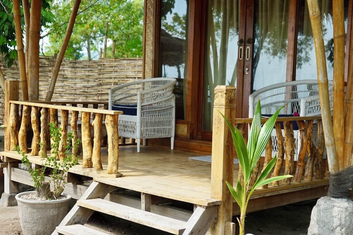 A wooden deck with a railing, two wicker chairs, and potted plants.