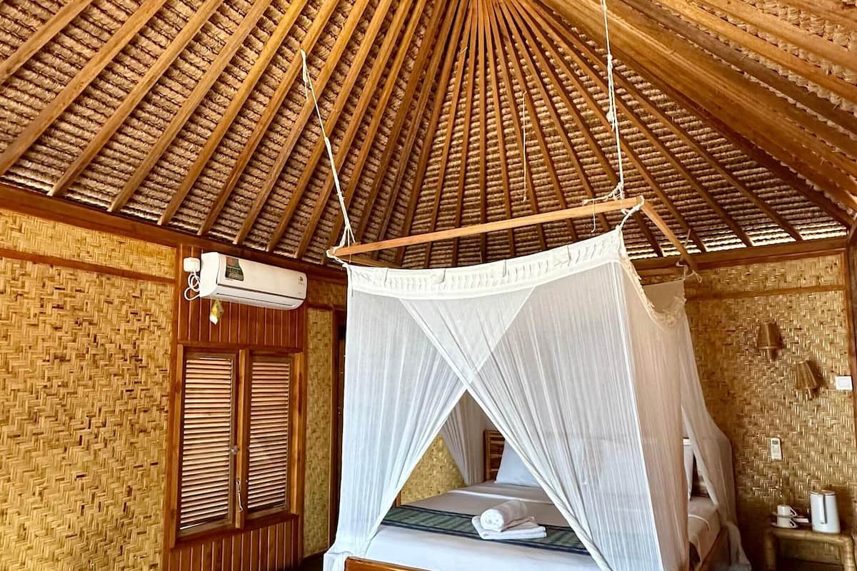 A room with a thatched roof, a bed with a canopy, and a woven wall.