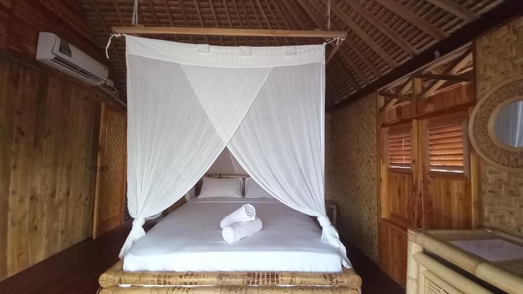 Un lit simple avec un baldaquin, des murs en bois, un plafond en bois et un petit miroir rond accroché au mur.