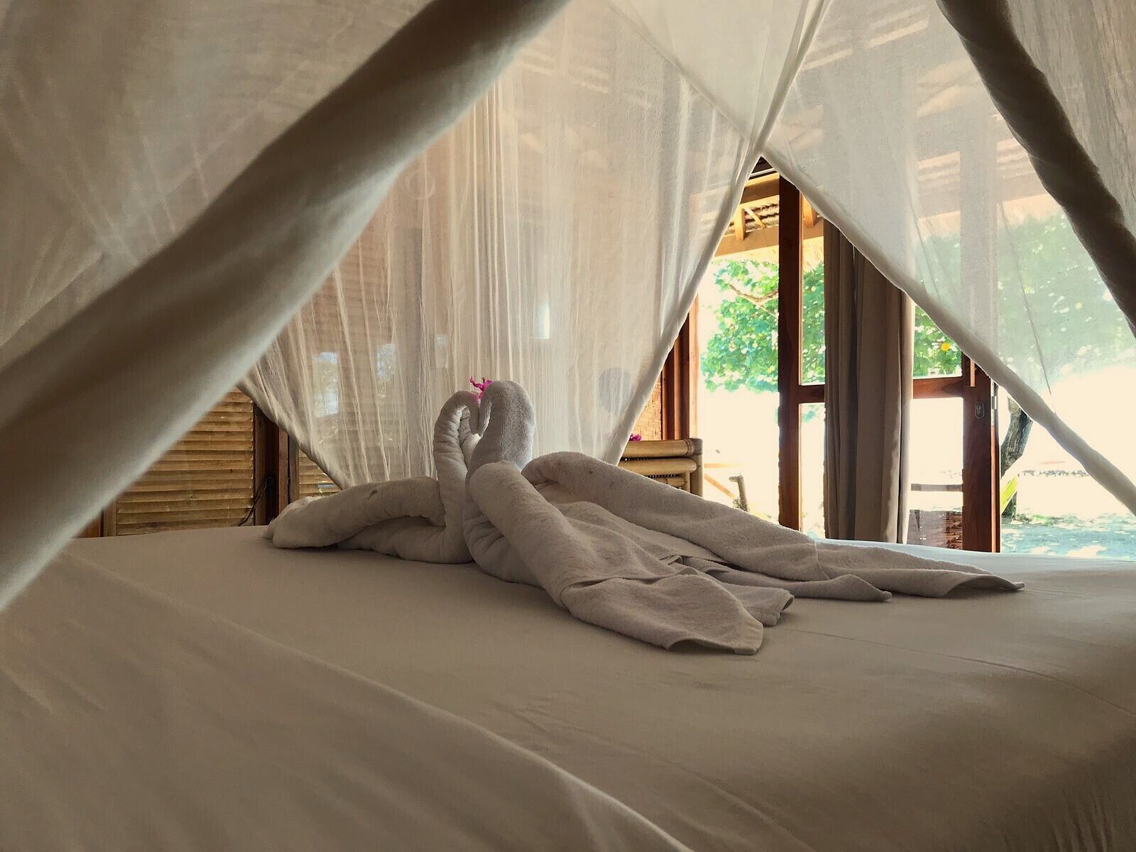 A bed with a canopy, a wooden structure, and a view of greenery outside.