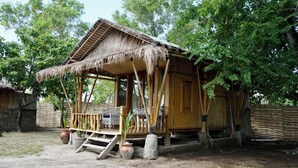 Une maison rustique en bois, avec un toit de chaume, une véranda en bois et un mur de pierre en arrière-plan.