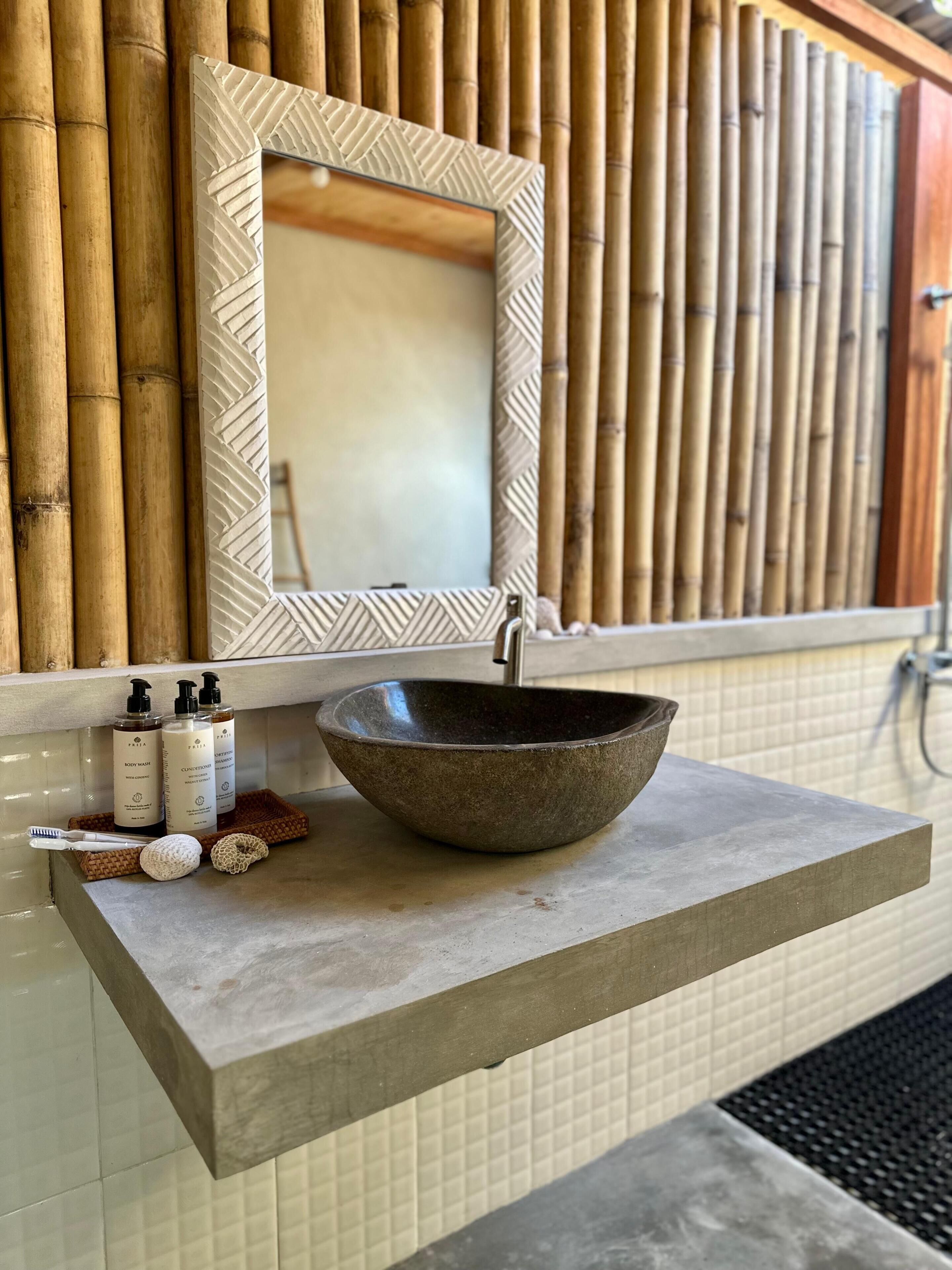 A bathroom vanity with a stone sink, a mirror with a geometric frame, and toiletries on a tray.