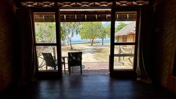 An open doorway to a beach area with two wicker chairs and a table, wooden flooring, and a view of the beach and ocean.