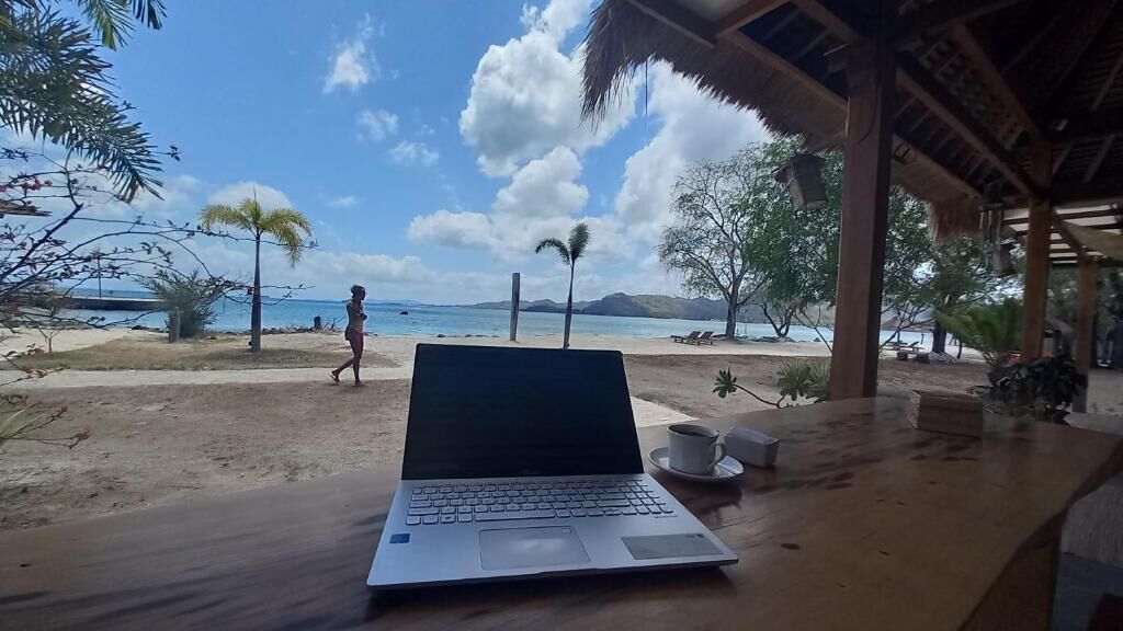 A laptop on a wooden table with a beach view, a cup, and a small box.