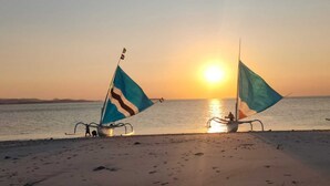 Une scène de plage avec deux voiliers au coucher du soleil.
