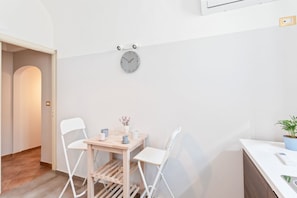 Habitación minimalista con pared blanca, una mesa de madera con dos sillas, un reloj y una planta pequeña.